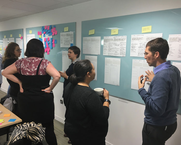 Group of five team members discussing annotated wireframes and content patterns during a co-design session.